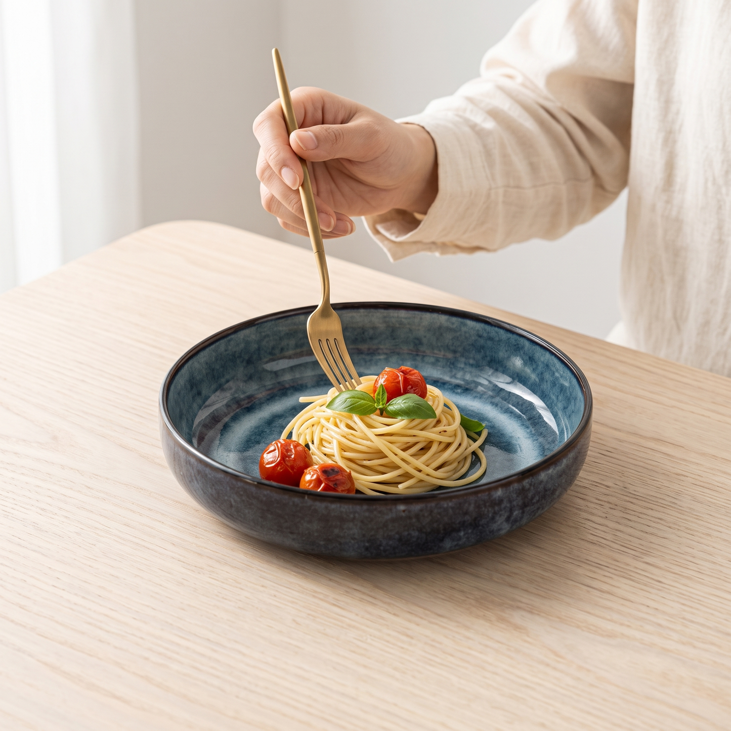 Aoi kiln-blue porcelain pasta plate on a pale oak table with pasta and a fork