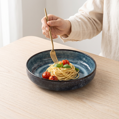Aoi kiln-blue porcelain pasta plate on a pale oak table with pasta and a fork